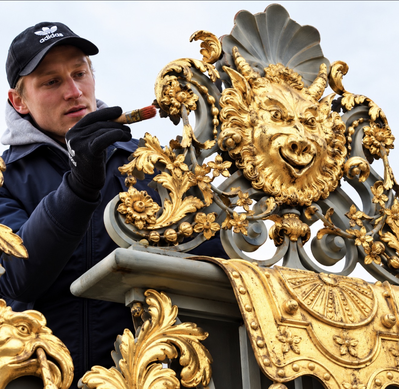 A craftsman working with a brush on historic gilded floral ornament beside a sculpted mask