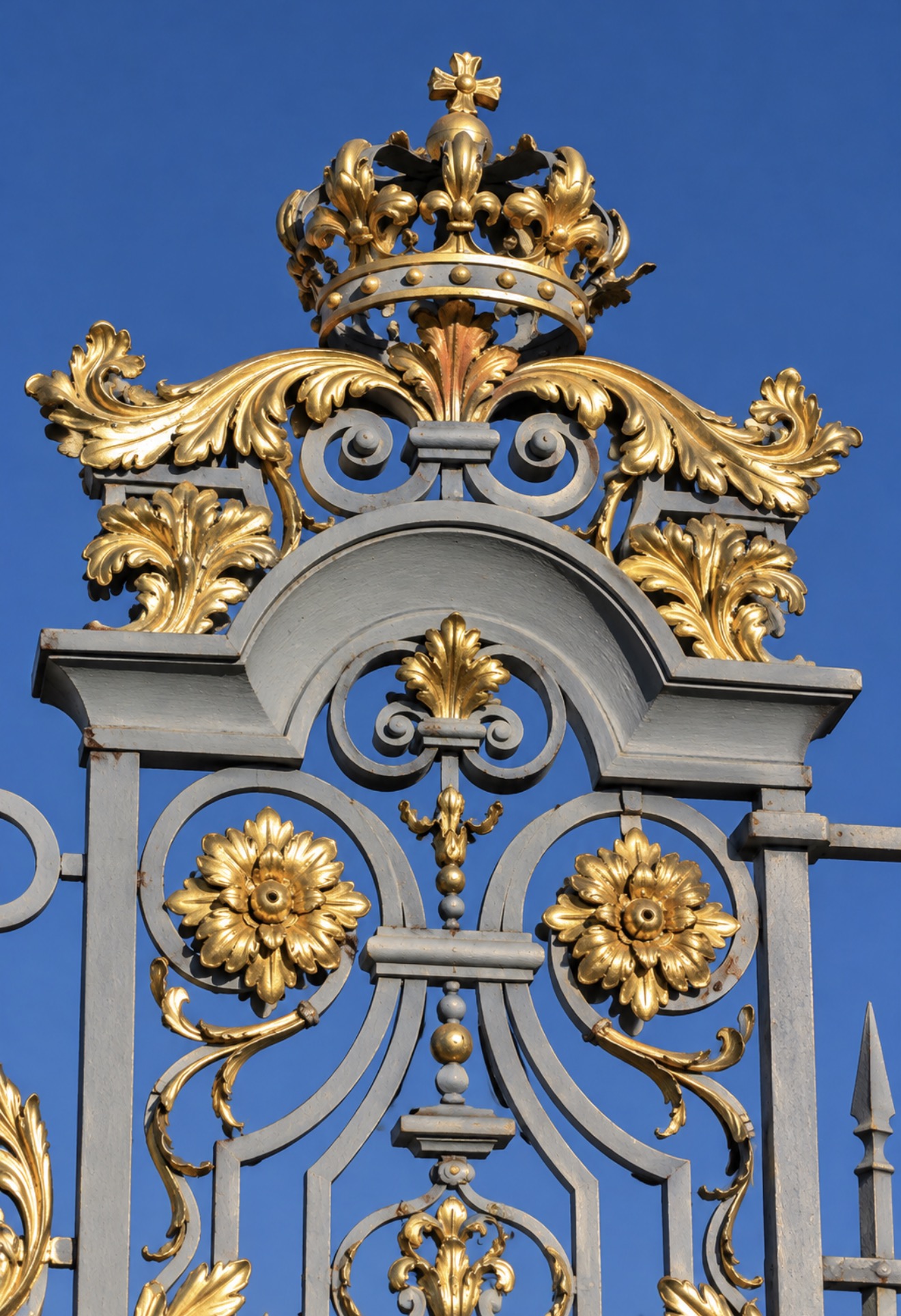 A gilded royal crown above scrolling ironwork and gold floral ornamentation